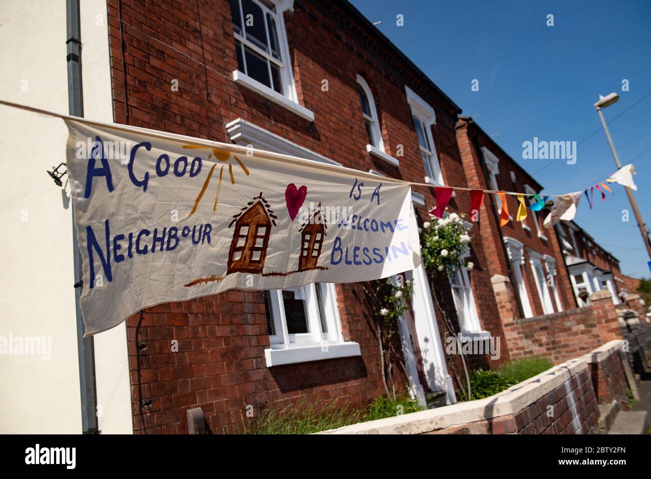 Duncombe Street a Wollaston, dove l'artista Luke Perry ha appeso bunting con messaggi di sostegno per i vicini e i lavoratori chiave, per creare un corridoio di 500 metri di colore attraverso il villaggio delle West Midlands. Perry ha chiesto ai residenti e ai negozianti locali di presentare disegni e messaggi, che poi dipinse a mano e cucì su conchettando con l'aiuto di volontari. Foto Stock