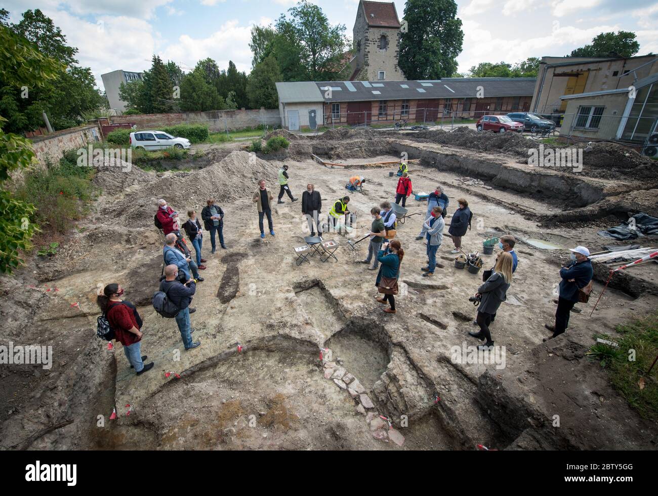 28 maggio 2020, Sassonia-Anhalt, Halle (Saale): I partecipanti ad una conferenza stampa dell'Ufficio di Stato per la conservazione dei Monumento e l'Archeologia si trovano nel mezzo di uno scavo archeologico nel Giardino Botanico. Durante gli scavi qui, i resti della ex chiesa del canonico monastero agostiniano Neuwerk sono stati trovati. I resti scoperti delle fondazioni rivelano un grande edificio della chiesa. Inoltre, sono state scoperte tombe di uomini, donne e bambini del Medioevo. La scoperta della posizione della chiesa è considerata come una sensazione archeologica che va oltre il suo r Foto Stock