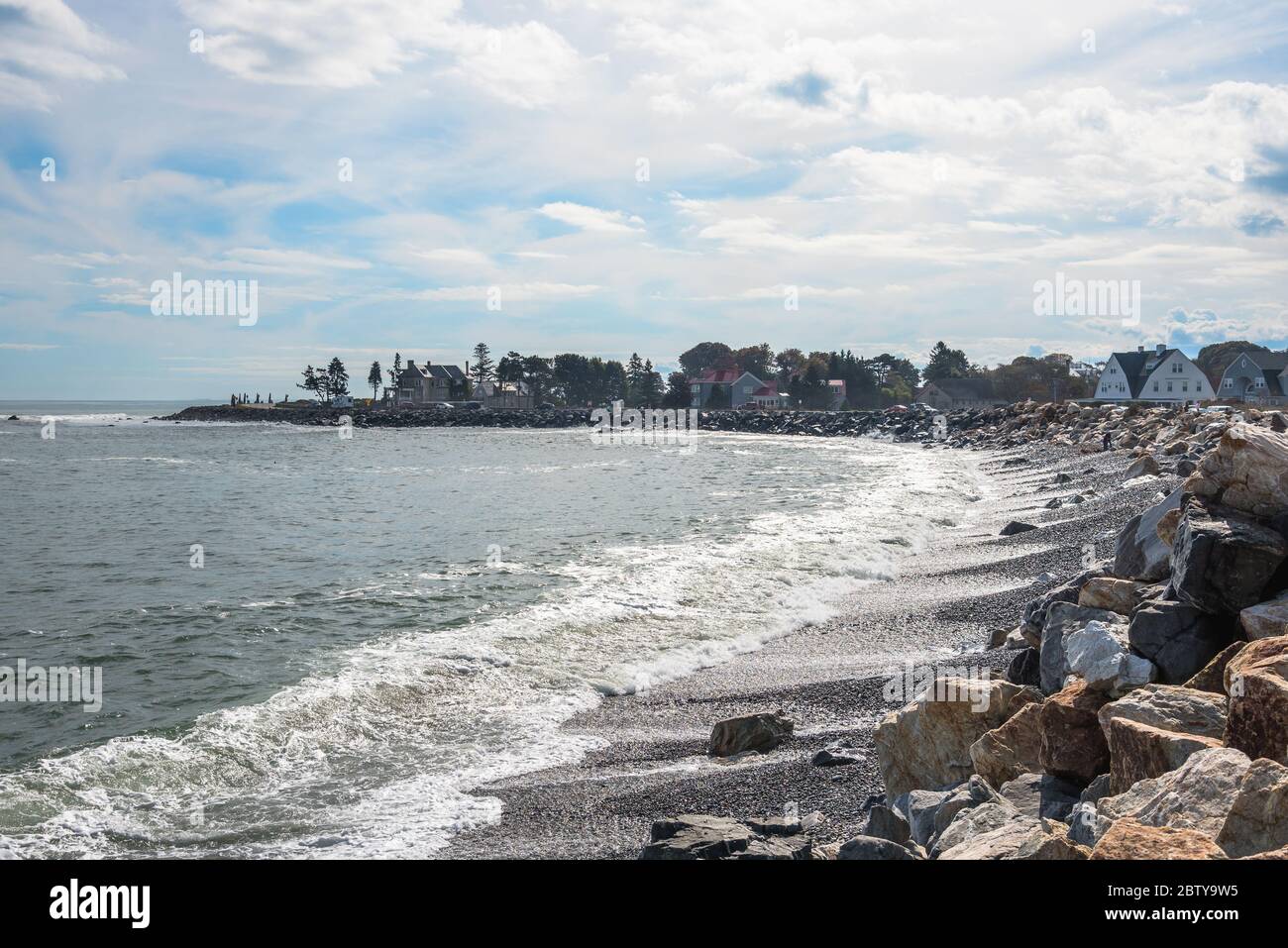 Cove e spiaggia di ghiaia lungo la costa del New Hampshire in una giornata soleggiata autunno. Una strada costiera fiancheggiata da edifici residenziali è visibile sullo sfondo. Foto Stock