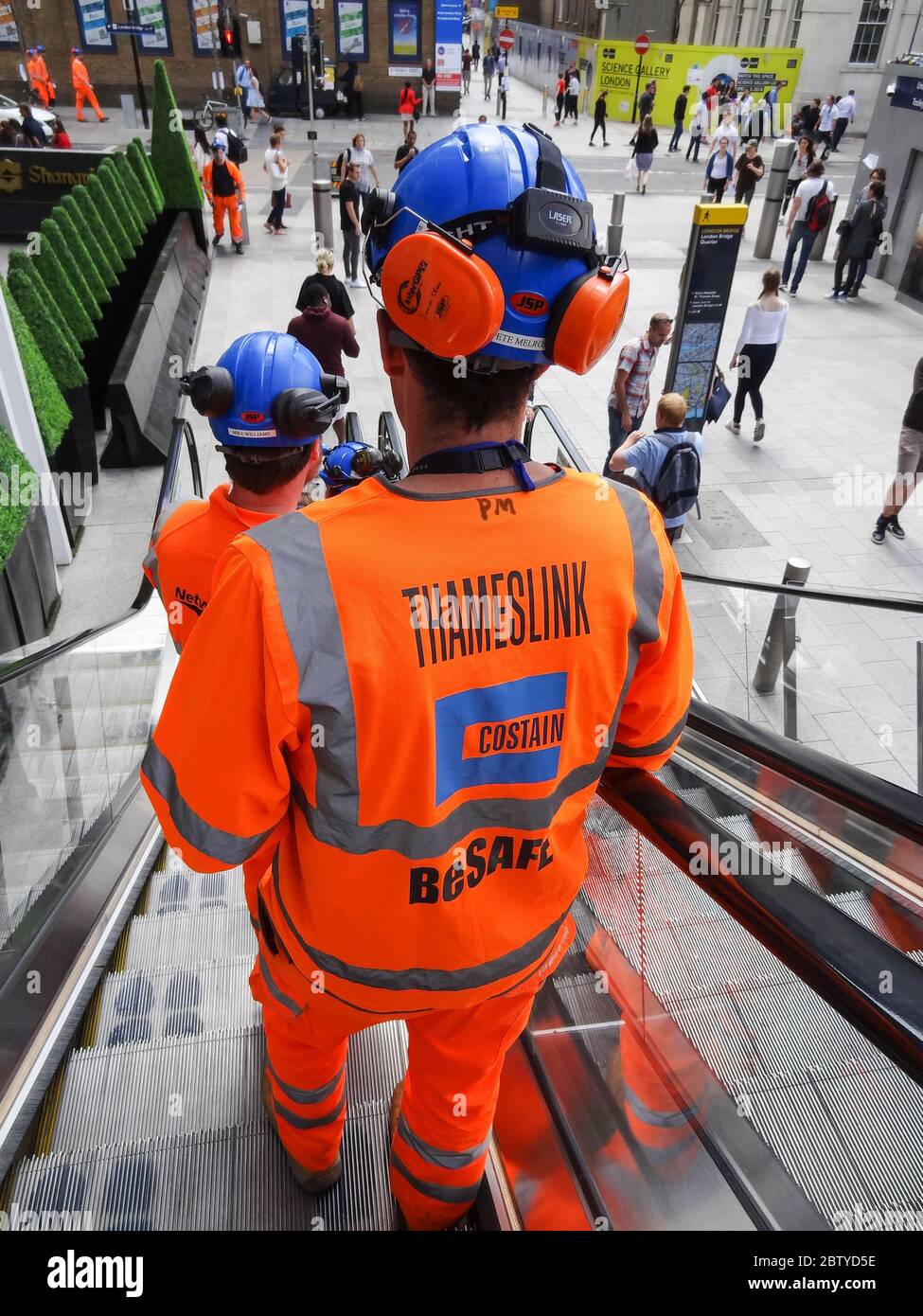 Un ingegnere di Thameslink Costain che scende da una scala mobile accanto alla stazione di London Bridge e allo Shard, Londra, Regno Unito Foto Stock