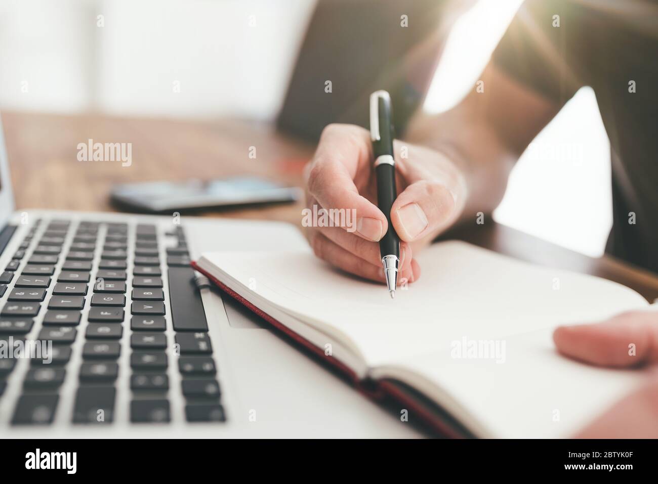 primo piano di una persona che prende appunti con la penna sulla carta davanti al computer portatile Foto Stock