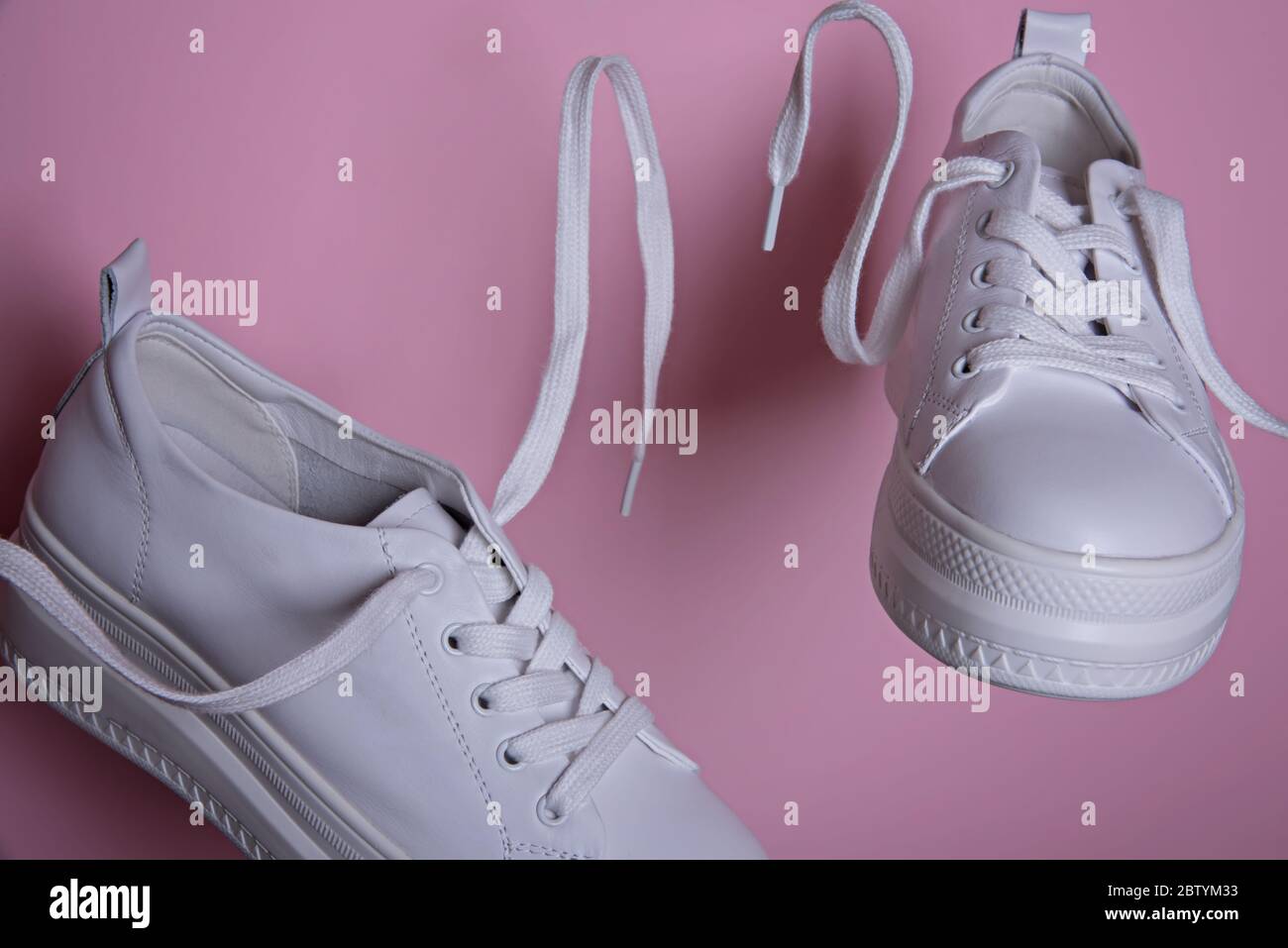 Sneaker bianche in aria su sfondo rosa. Surrealismo astratto e minimalismo concetto di shopping. Foto Stock