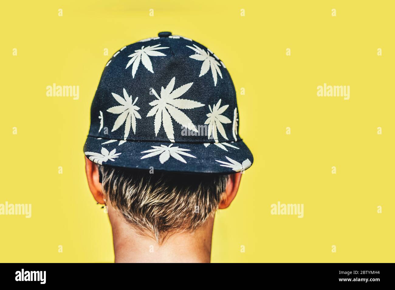 Ragazza in occhiali da sole e cappello con foglie di marijuana fuma su sfondo giallo Foto Stock