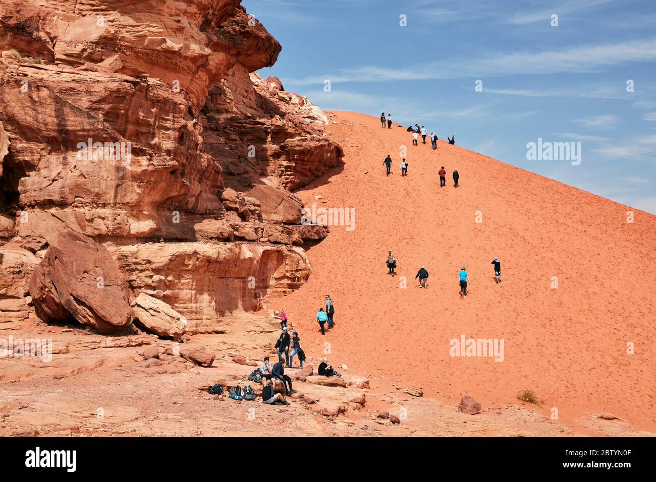 Turisti che arrampicano duna di sabbia a Wadi Rum, Aqaba, Giordania Foto Stock