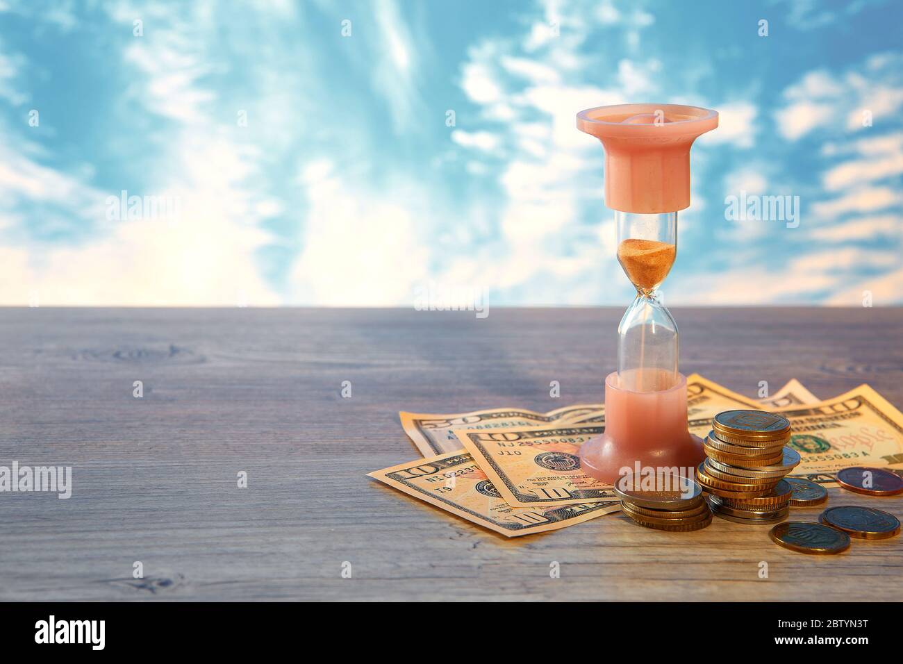 Il tempo è denaro. Concetto finanziario di denaro con un orologio e monete di paesi diversi. Clessidra. Foto Stock