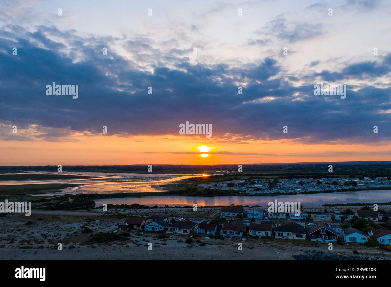 Splendido tramonto sulla Riserva Naturale di Pagham con il sole che affonda verso l'orizzonte e i colori che si riflettono al largo del lago. Vista aerea. Foto Stock Splendido tramonto sulla Riserva Naturale di Pagham con il sole che affonda verso l'orizzonte e i colori che si riflettono al largo del lago. Vista aerea. Foto Stock