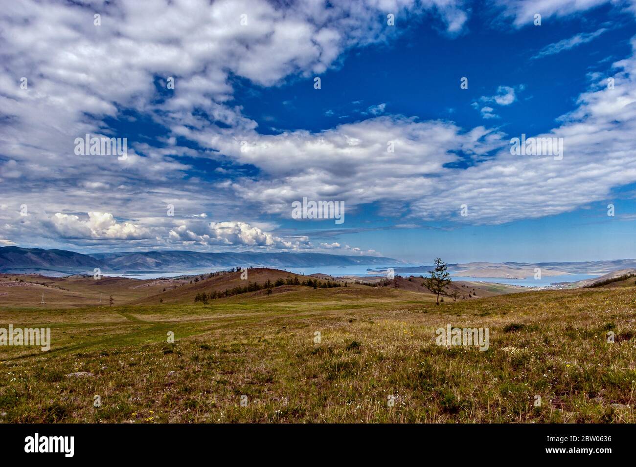 Incredibile paesaggio di colline vicino al lago Baikal e nuvole contro un cielo blu. Erba verde sul terreno. Lontano le montagne. Orizzontale. Foto Stock