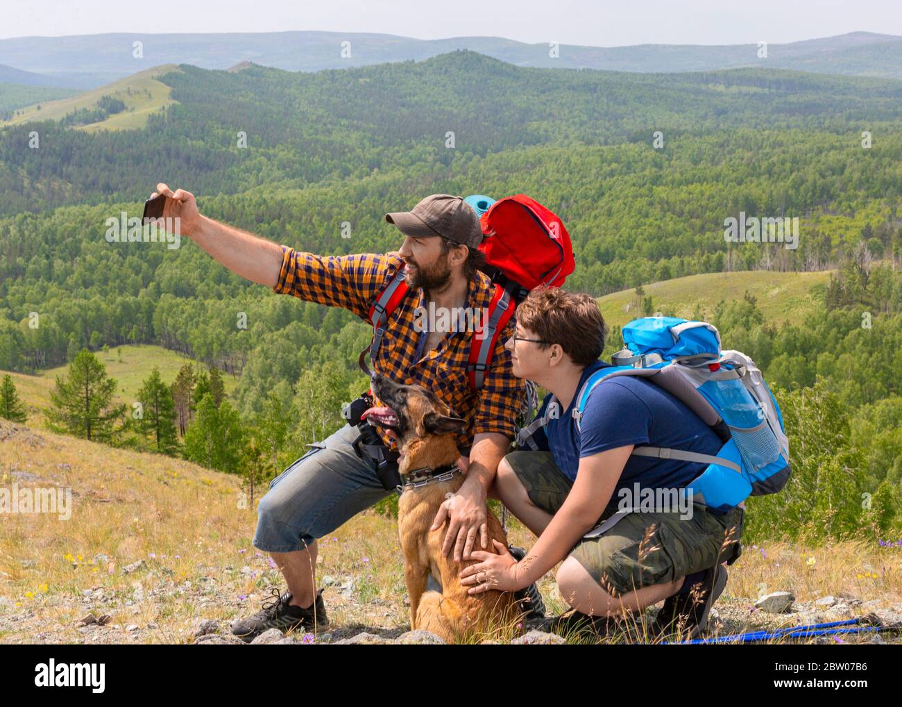 Padre con figlio e il loro cane prendono un selfie sulla cima della montagna. Il concetto di aumentare l'amore per gli animali domestici e uno stile di vita attivo. Foto Stock