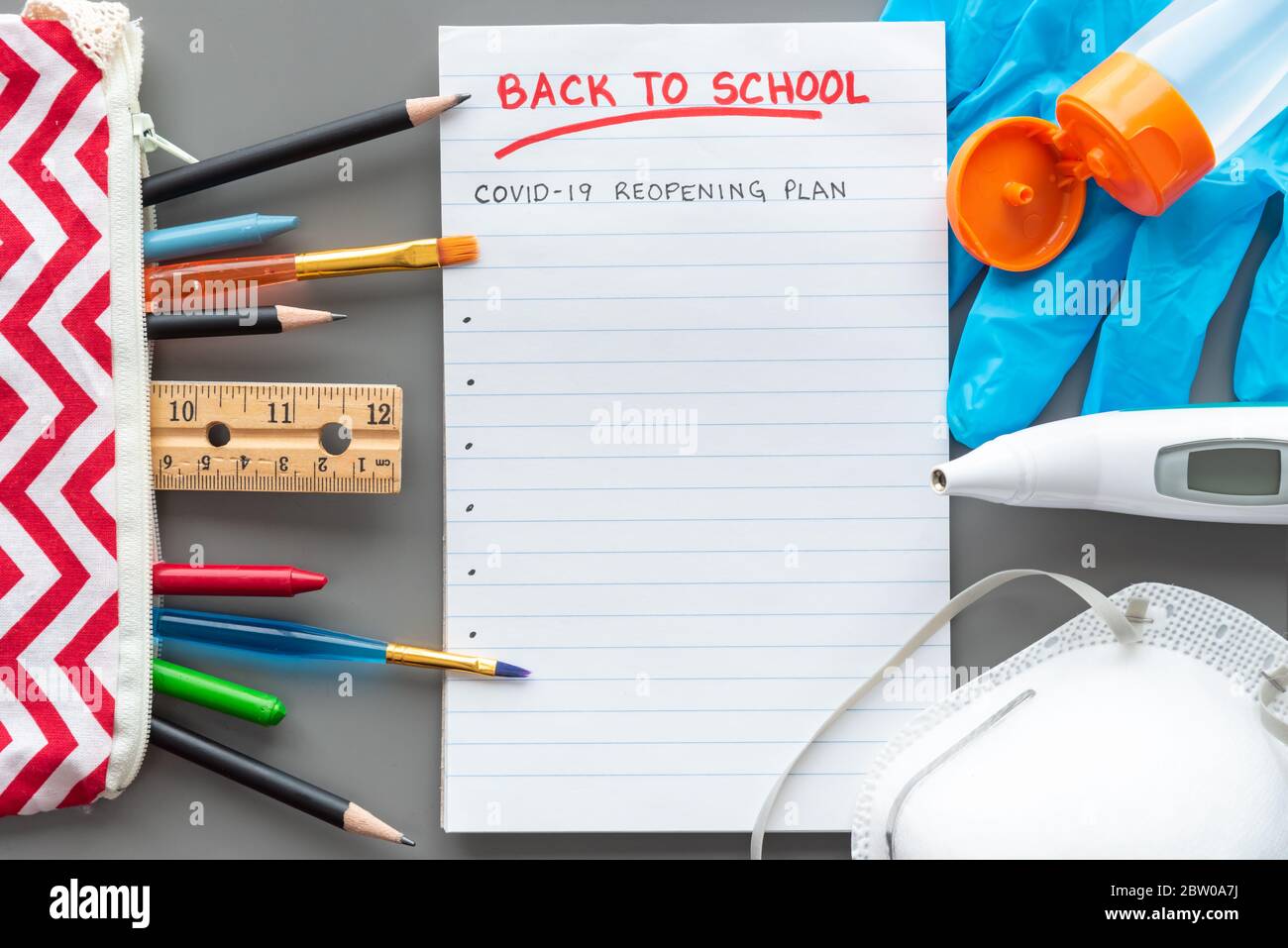 Appartamento di ritorno a scuola su sfondo grigio con forniture scolastiche e attrezzature mediche. Foto Stock