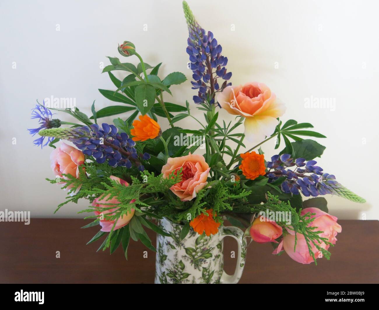 Una disposizione di fiori recisi estivi in una caraffa, caratterizzata da  lupini viola e rose color albicocca Foto stock - Alamy