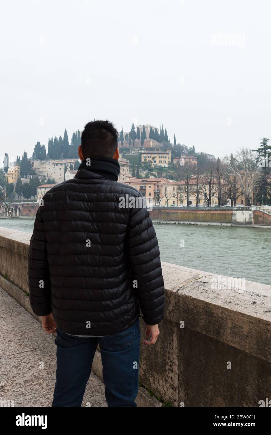 Immagine verticale della schiena del giovane guardando all'orizzonte di Verona durante una giornata fredda, Italia Foto Stock