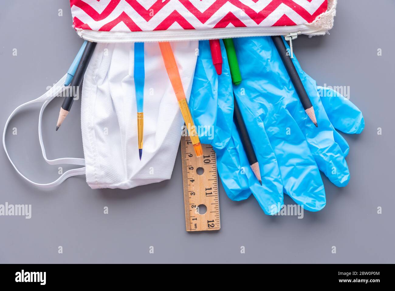 Ritorno a scuola durante la pandemia del coronavirus COVID-19. Custodia a matita per bambini piena di materiale scolastico, guanti e maschera facciale. Foto Stock