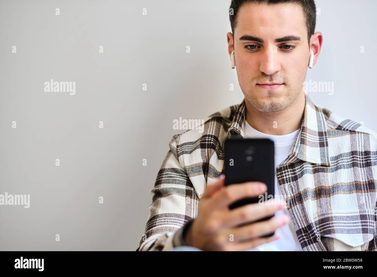Giovane uomo con auricolari che guardano lo smartphone. Rilassarsi a casa. Spazio di copia. Foto Stock