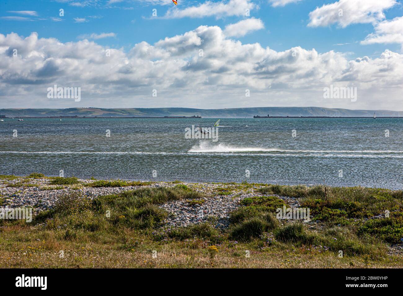 I windsurfisti praticano una bella mattina soleggiata sulle acque della baia di Weymouth contro un cielo blu nuvoloso Foto Stock