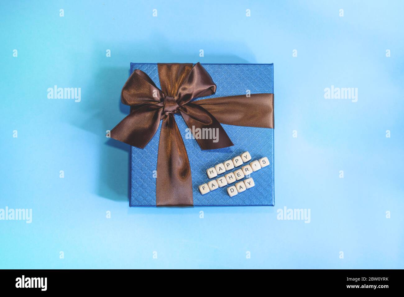 Un regalo blu con striscia marrone su sfondo blu. Un segno di buon giorno del Padre da blocchi di legno. Concetto di festa del Padre. Foto Stock