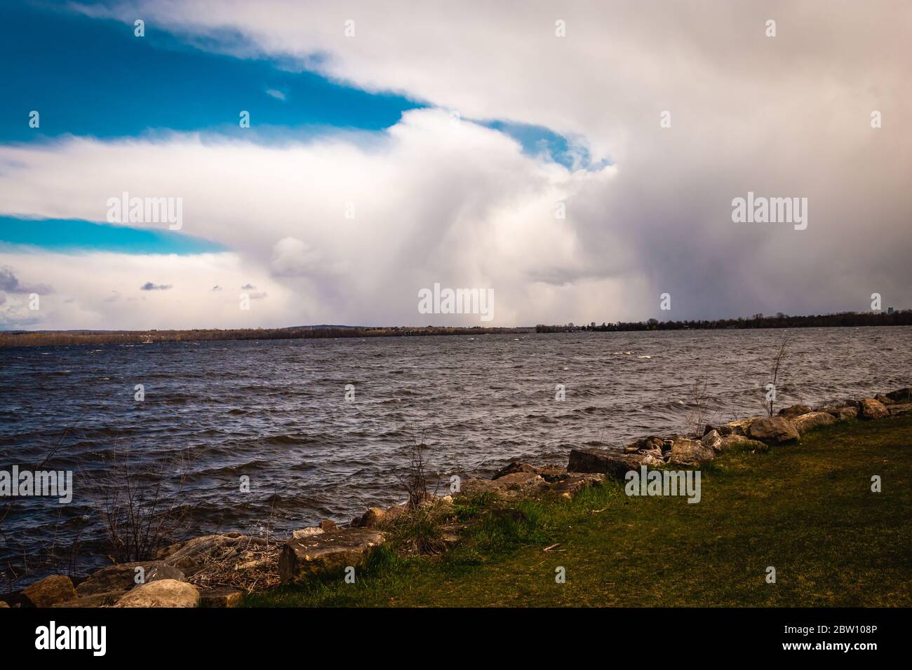 Le fitte nuvole bianche, con le parti più scure che mostrano pioggia in lontananza, si intrecchiano sul cielo blu sopra un fiume Ottawa in Canada. Foto Stock