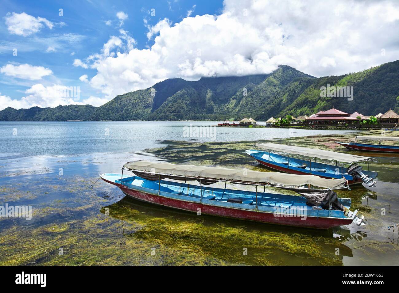 Barche turistiche che si appoggiano sul bordo del lago Batur sullo sfondo di montagne e molto bello cielo blu nuvoloso. Kintamani, Bali, Indonesia Foto Stock