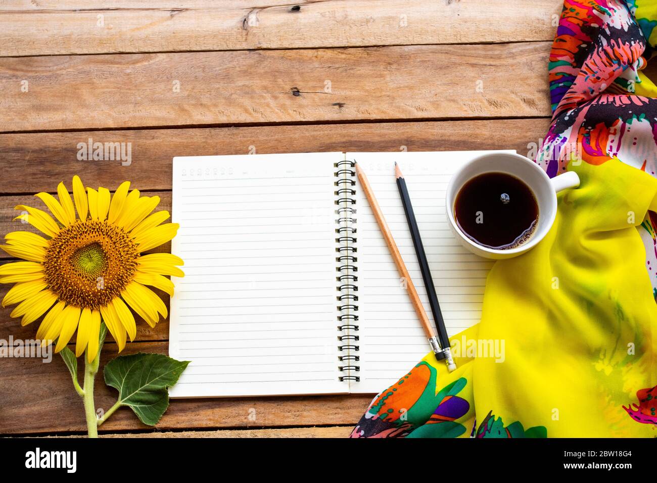 notebook planner per lavoro di affari con caffè caldo, fiori gialli girasole, disposizione sciarpa piatto stile di posa su sfondo legno Foto Stock