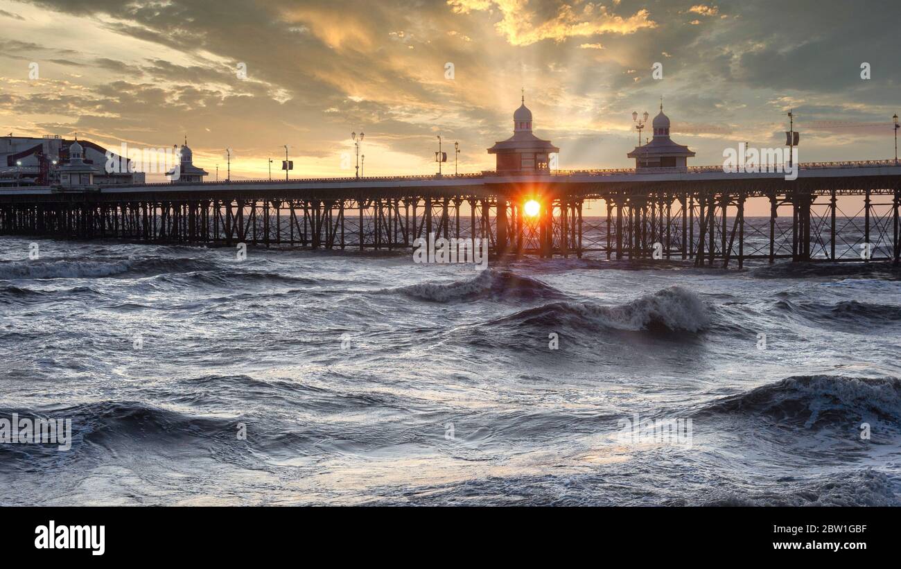 Il sole tramonta sotto il molo con i raggi del sole. La fotografia mostra il molo nord di Blackpool e un mare ruvido Foto Stock
