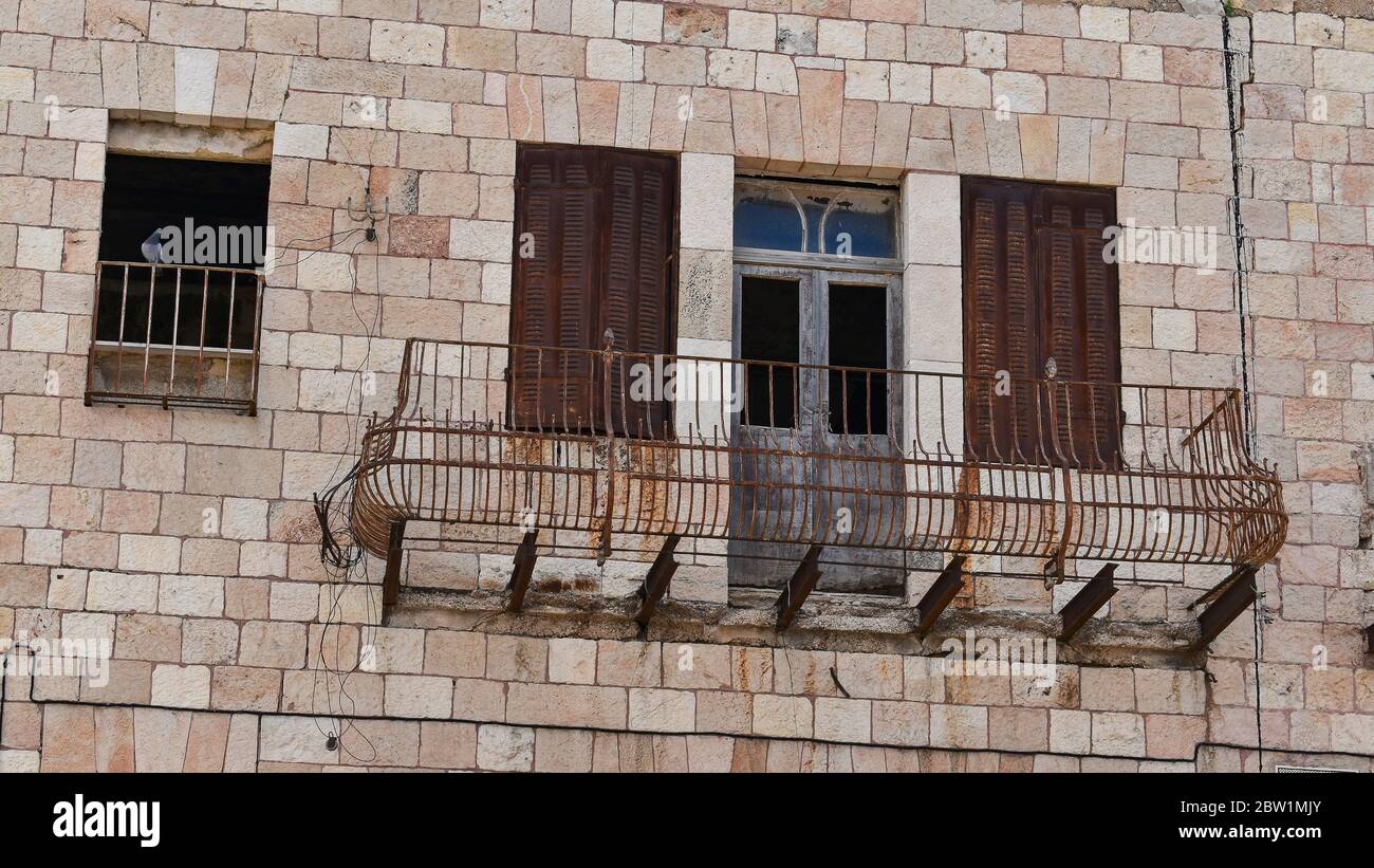 un piccione sembra ispezionare un pericoloso vecchio balcone di ferro arrugginito trascurato su un edificio di pietra calcarea a gerusalemme in israele Foto Stock