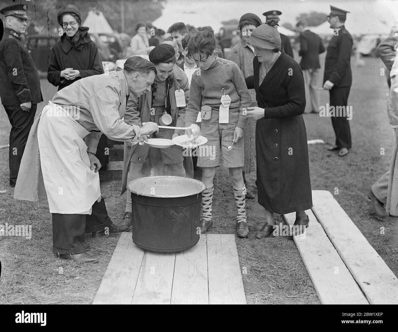 Rifugiati bambini da spray primo buon pasto in mesi al campo di Southampton. Dopo lo sbarco dal liner Habana che li portò dalla zona della guerra civile a Bilbao, i 4000 bambini rifugiati sono stati portati nel campo speciale fuori Southampton e hanno dato il loro primo pasto decente in molti mesi. Hanno vissuto sul pane nero e soffrono per la paura perpetua delle incursioni aeree. Foto mostra, i bambini rifugiati che ricevono il loro primo pasto dalle cucine alimentari al campo di Southampton oggi (Domenica). 23 maggio 1937 Foto Stock