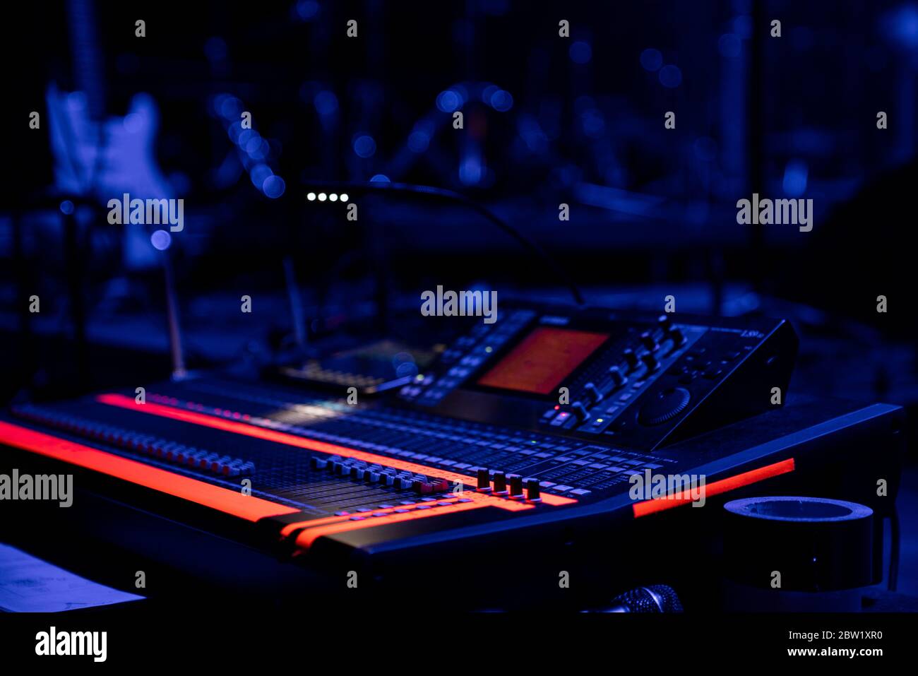 Console di mixaggio audio in caso di fulmini in un luogo di concerto con una chitarra in background Foto Stock