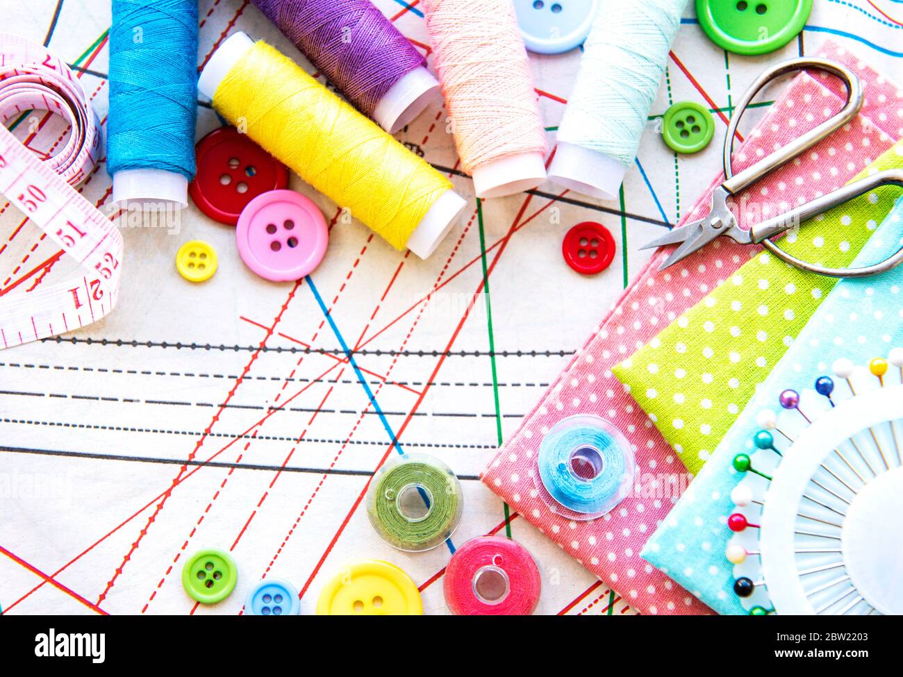 Accessori per cucire e tessuti su un tavolo. Fili da cucire, aghi, spille, tessuti, bottoni e centimetro da cucire. Vista dall'alto, disposizione piatta. Foto Stock