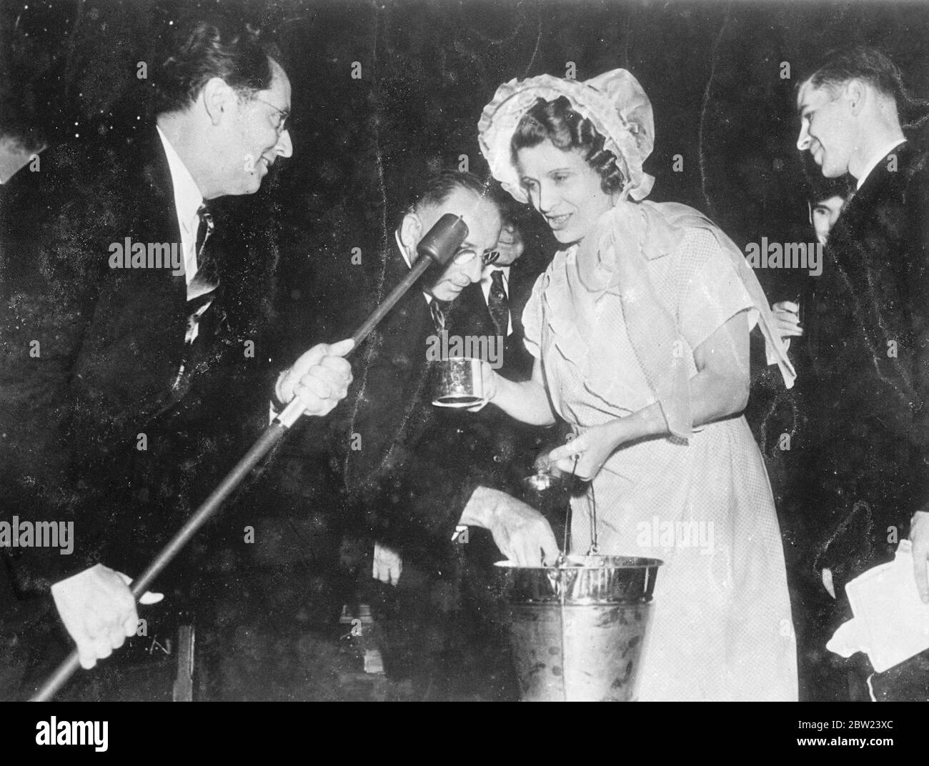 Vestito in costume di milkmaid - ricordando la sua giovinezza in una fattoria in Canada - Aimee Semple McPherson (il gospeler caldo/evangelista dell'America) ha dato una festa di quarantesimo compleanno nel Tempio di Angelus a Los Angeles, California. hanno partecipato 6000 persone. Spettacoli fotografici: Aimee Semple McPherson che dà tazze di latte ai suoi ospiti. Tenere un microfono è un Cavaliere Giles. 17 ottobre 1938 Foto Stock