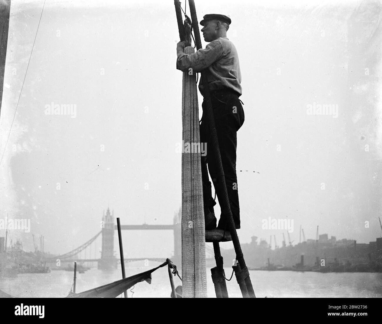 Un marinaio, pescatori che arrampicano su un albero su una barca, nave sulla piscina di Londra, il Tamigi con il Tower Bridge sullo sfondo. 1933 Foto Stock
