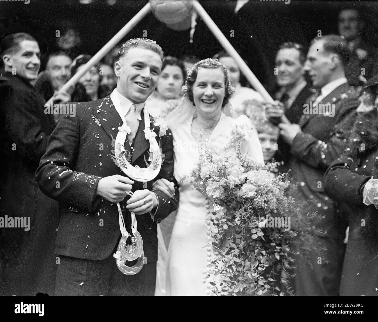 Arco di bandiere d'angolo per il calciatore Fulham e la sua sposa. Trevor Smith, il Fulham dentro a destra, è stato sposato con la signorina Lillian Boyce di Wimbledon alla Trinity Church, Wimbledon. Dopo la cerimonia, Smith si è rivelato per Fulham contro Plymouth Argyle a Craven cottage. Foto mostra, lo sposo indossando un cavallo per fortuna, mentre ha lasciato la chiesa con la sposa. 1 gennaio 1938 Foto Stock