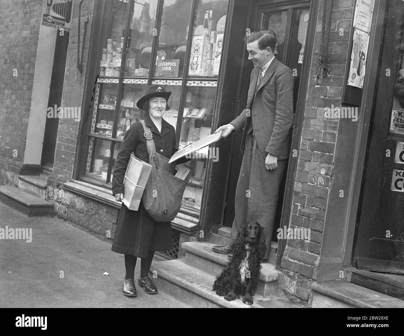 Una donna che cammina Ufficio postale a Kent. La sig.ra Grace Coles, di Wrotham, Kent, è una postdonna ausiliaria e un ufficio postale di viaggio pure. Ha camminato miglia ogni giorno consegnando le lettere alle persone che vivono in zone remote di North Kent Downs, e inoltre vende i francobolli e gli ordini postali su di lei e scatta le lettere e pacchi dalle case. Il suo giro inizia sulla strada del Pilgrim e termina al Labor in Vain Hill. Cammina per più di 2500 miglia all'anno. Spettacoli fotografici, Miss Grace Coles che consegna un pacco a un abitante di un villaggio a Wrotham, Kent. 7 dicembre 1937 Foto Stock