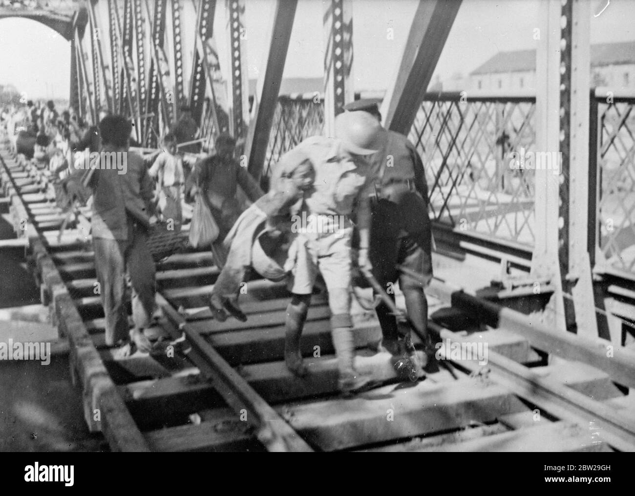 Briton si è assicurato di salvare una vita!. I rifugiati si riscaldano sul ponte come ritiro cinese da Shanghai. Un soldato britannico, con un piccolo rifugiato cinese sotto il suo braccio, precipita attraverso il ponte ferroviario Jessiefield a Shanghai dopo essere stato parzialmente distrutto dai cinesi in ritirata. Il ponte si trova sulla ferrovia Shanghai-Hangchow. I rifugiati si sono impigliati migliaia sul ponte e sono battuti alle porte dell'insediamento internazionale che ha pregato di essere ammessi. A volte, le forze che sorvegliavano il confine nord-occidentale dell'insediamento erano quasi impotenti contro le folle terrorizzate che spazzarono d Foto Stock