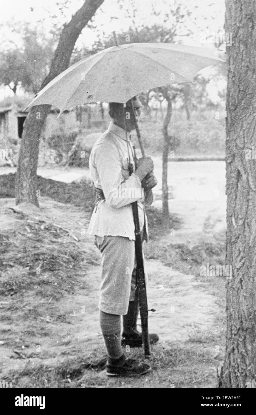 Ritirarsi dai cinesi lascia dietro di loro un muro di fuoco a Shanghai. Martoriato da mesi di bombardamenti e bombardamenti, Chapei, il quartiere cinese di Shanghai, divenne un inferno infuriato quando fu licenziato dalle truppe cinesi mentre si ritirarono prima dei vittoriosi giapponesi. Foto mostra, soldato cinese con un ombrello per proteggerlo dalla pioggia. 1 dicembre 1937 Foto Stock