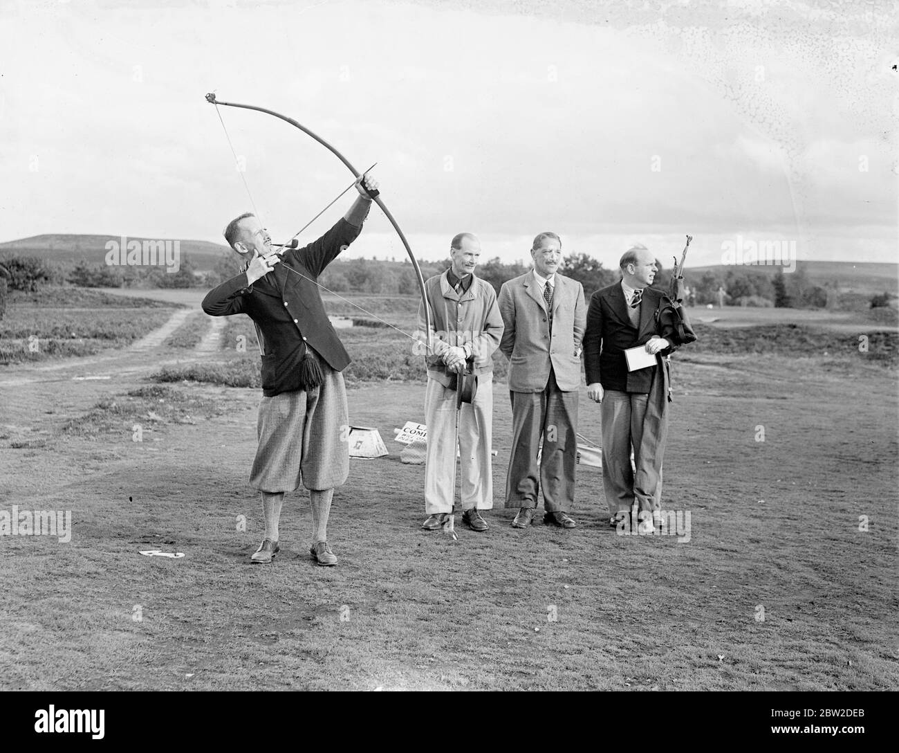 Giocando con arco e freccia, il maggiore J G Hayter, riconosciuto esperto dello sport annuale di prua e freccia di golf, ha incontrato il colonnello e St George Kirke, il capitano del club, in una partita al Hankley Common Golf Club, Surrey. Ha ammesso un colpo una balla. Major Hayter spara la sua freccia in una scatola invece di un buco. La sua media per la maggior parte dei corsi di Surrey è negli anni settanta. Spettacoli fotografici: Il maggiore J G Hayter spara, guardato dal suo avversario, col e St George Kirke. 18 ottobre 1938 Foto Stock