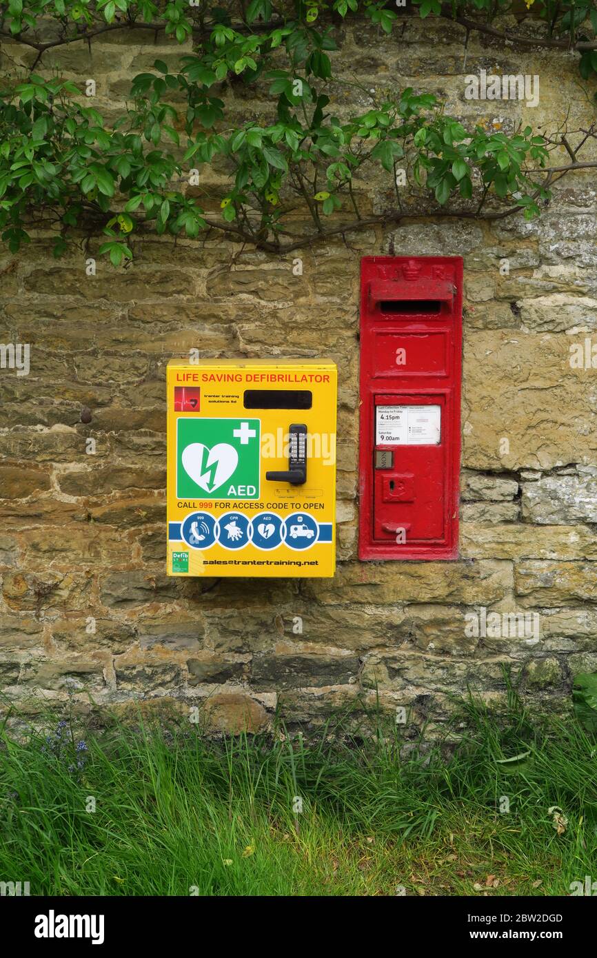 Defibrillatore e scatola di posta vittoriana montata su una parete nel villaggio Warwciskhire di Ascott Foto Stock