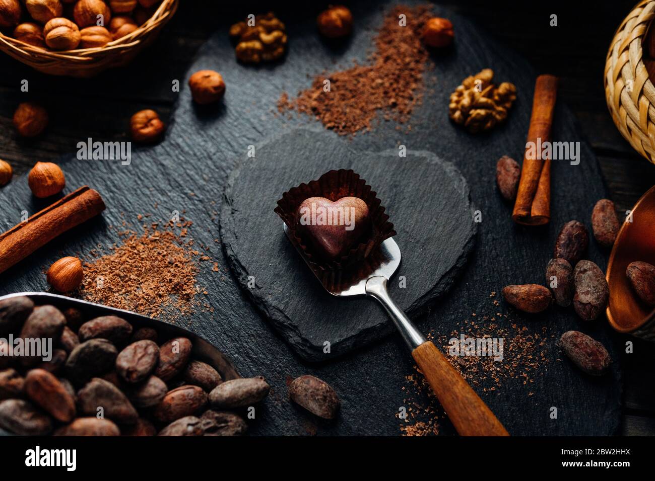 Caramella di cioccolato fatta a mano nella forma di erba all'interno dell'involucro di caramella . Caramelle al cioccolato su spatola e blackstone si stazionare a forma di cuore con fagioli di cacao, noci Foto Stock