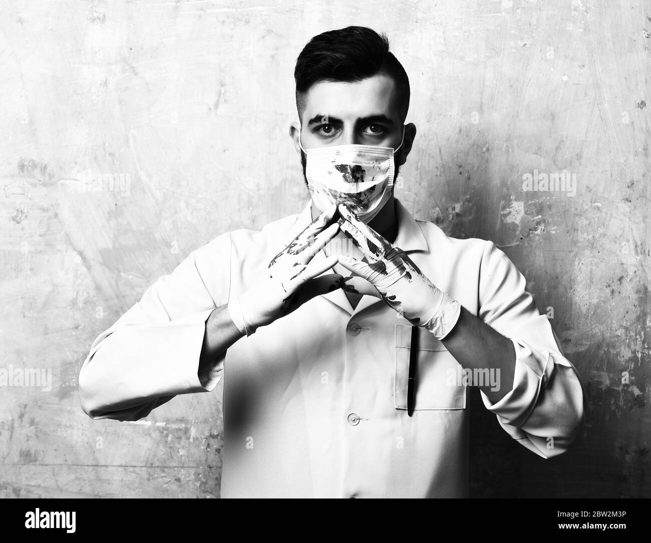 Chirurgo con elegante taglio di capelli in maschera macchiata con sangue  tiene le mani in guanti insieme sullo sfondo di colore beige parete Foto  stock - Alamy