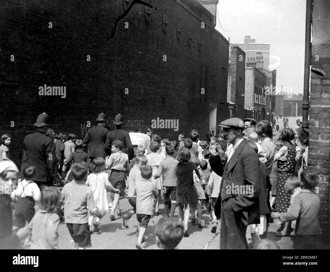L'East End di Londra. I bambini locali seguono i poliziotti in fondo alla strada. 1933 Foto Stock