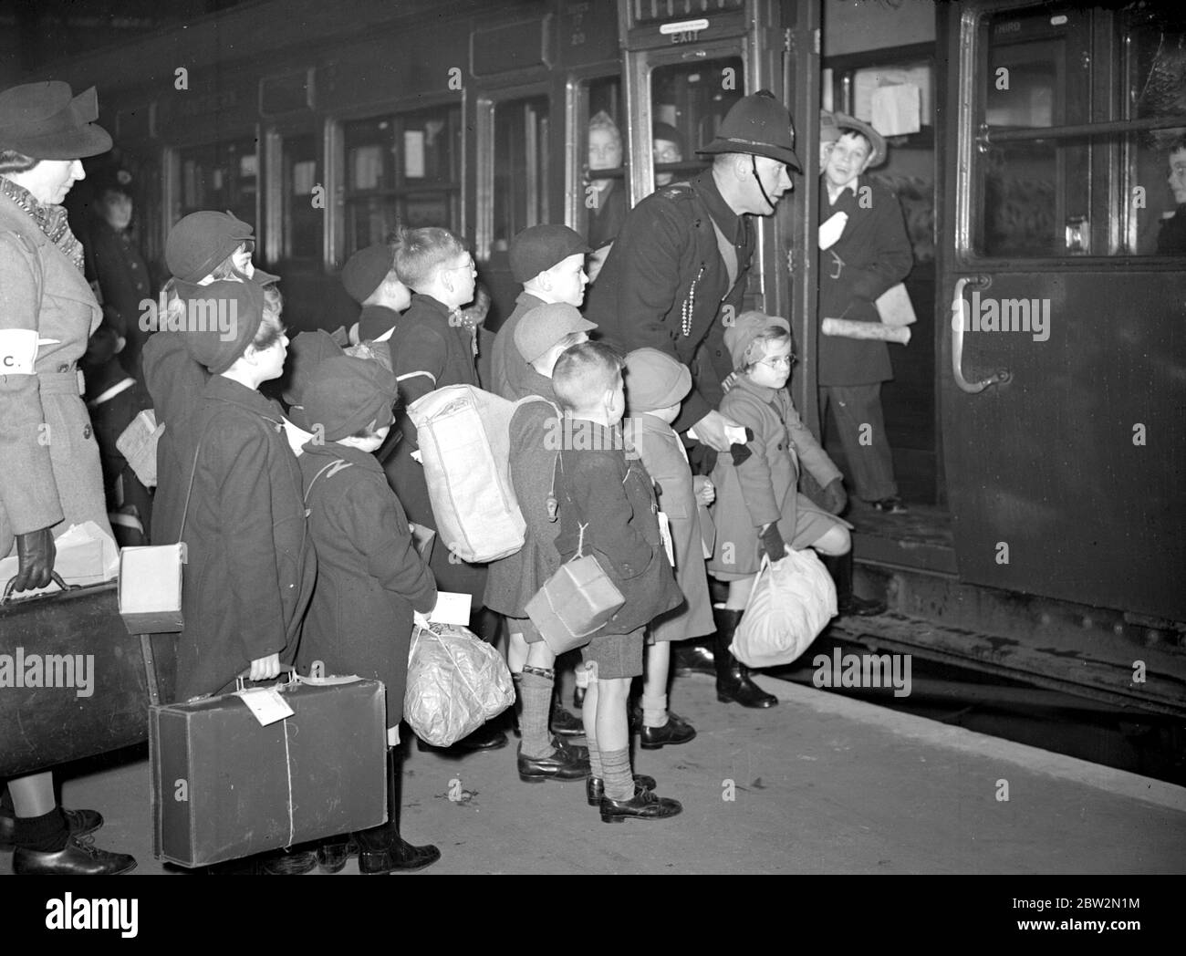 Crisi di guerra, 1939. Le precauzioni contro i RAID aerei iniziarono la seconda guerra mondiale e gli evacuati, come questi in questa foto, iniziarono a riversarsi fuori Londra per la sicurezza delle campagne. Trasportando le casse della maschera a gas, le etichette dei bagagli che le identificano, fissate ai loro vestiti, era per alcuni di loro una grande avventura, perché molti di loro non avevano mai lasciato la sede, o persino Londra prima. Bambini che partono per Devon. 14 dicembre 1939 Foto Stock