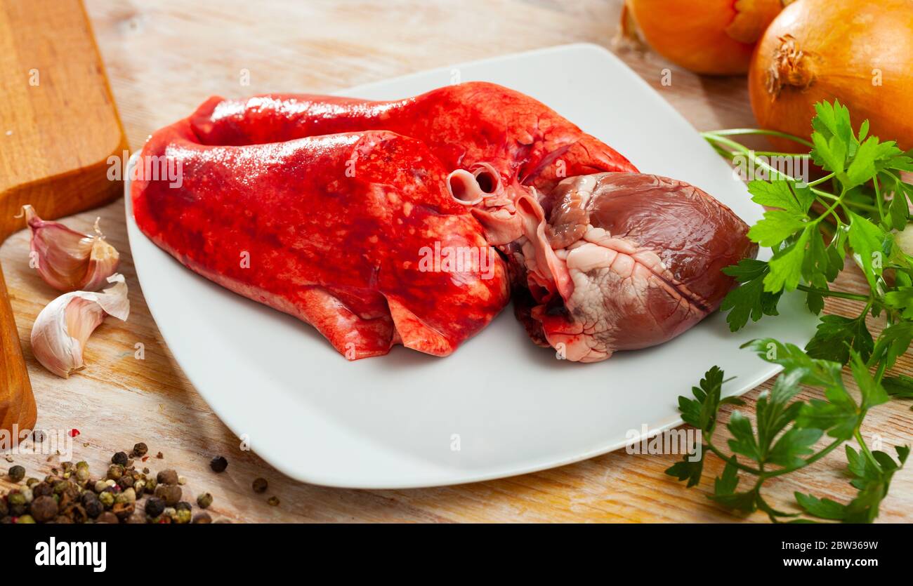 Ingredienti per cucinare. Polmoni grezzi di montone e cuore con cipolla, aglio, spezie ed erbe su tavola di legno Foto Stock
