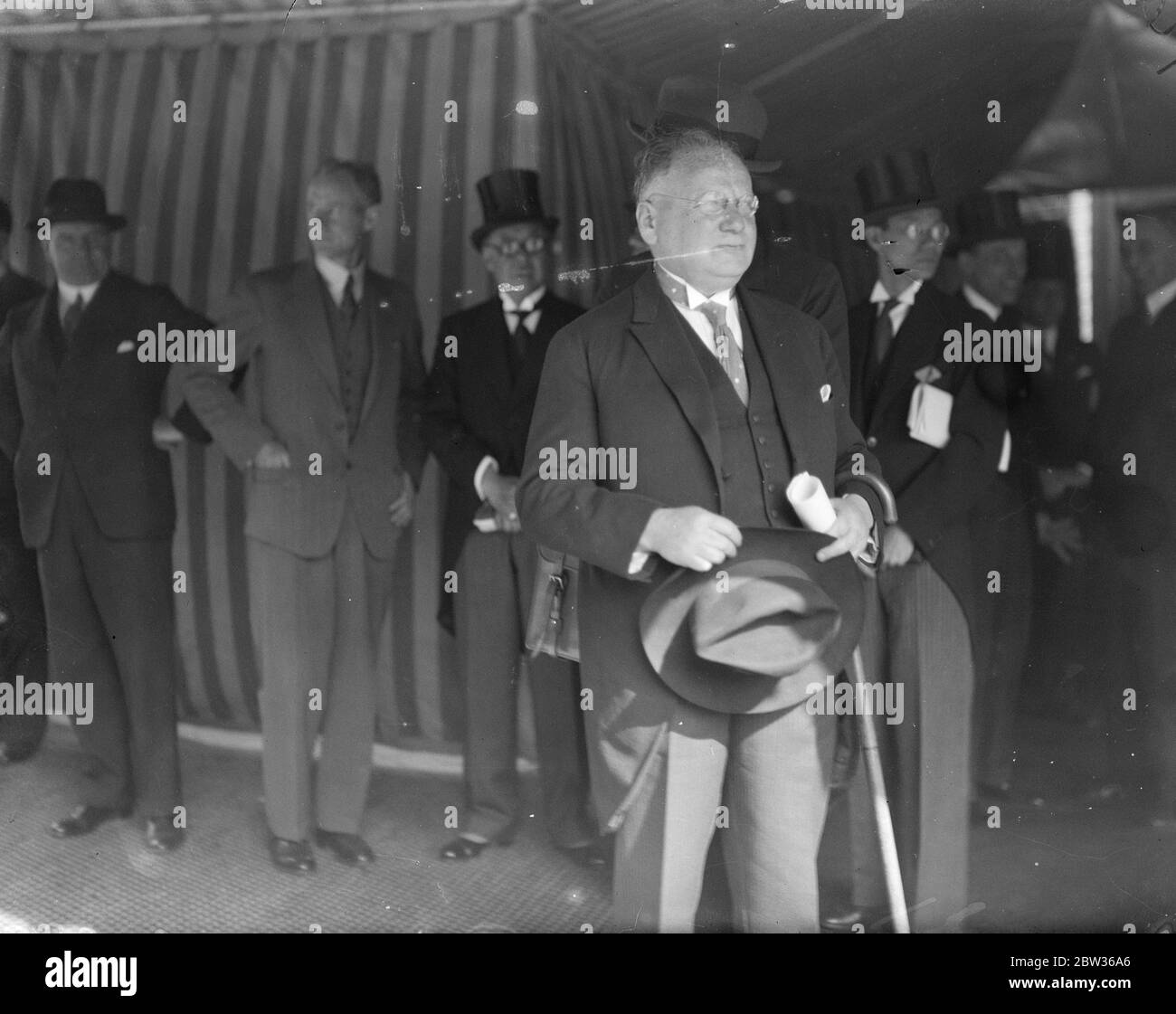 Tenda a righe e uomini in top cappelli e code - uomo in primo piano con cappello trilby e bastone a piedi in mano - Litvinoff alla conferenza economica . 1933 Foto Stock