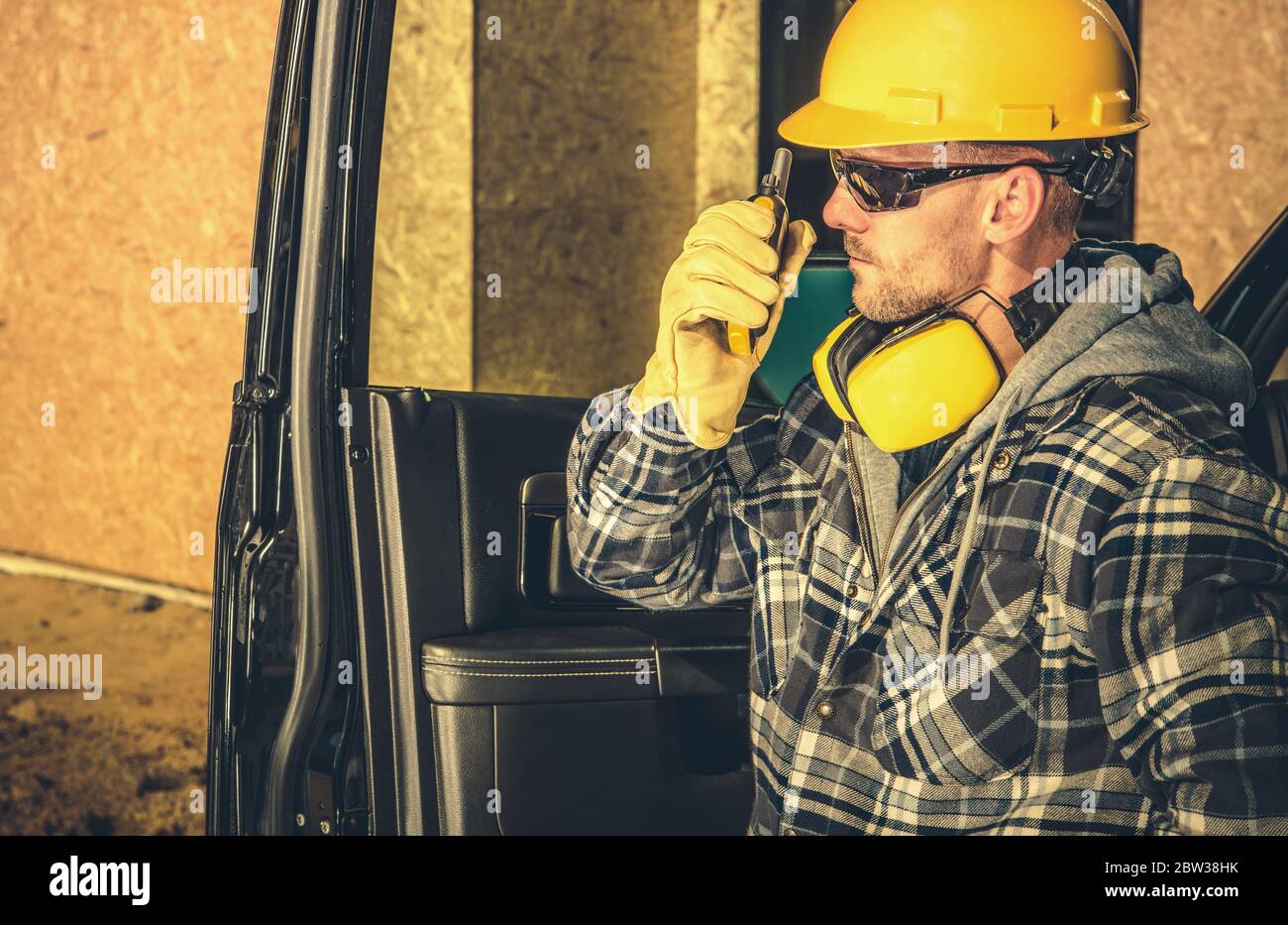 Appaltatore caucasico che effettua una conversazione rapida in loco con altri lavoratori che utilizzano Walkie Talkie mentre si siedi al suo veicolo aziendale. Costruzione Foto Stock