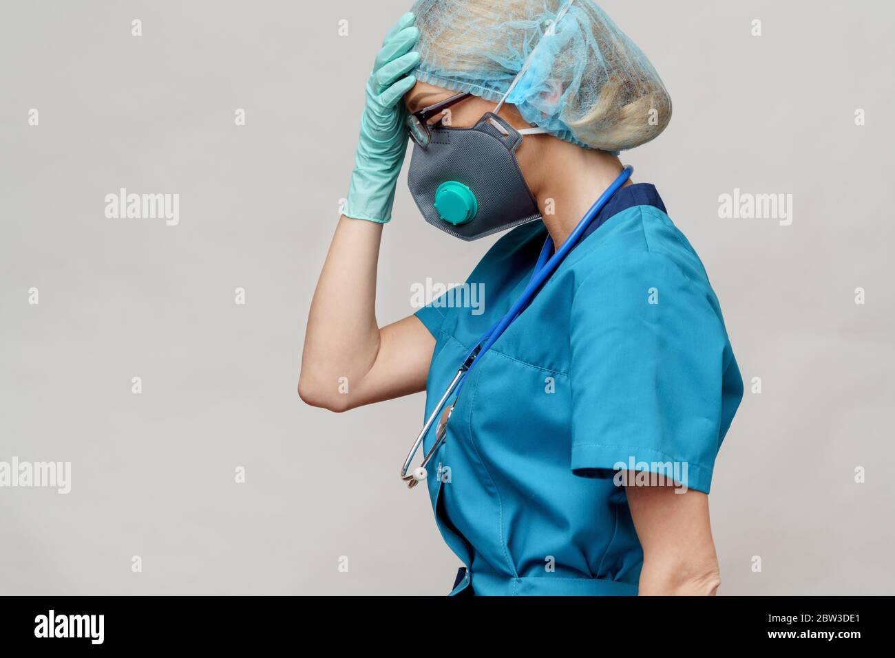 medico femminile con stetoscopio che indossa maschera protettiva e guanti in lattice su sfondo grigio chiaro Foto Stock