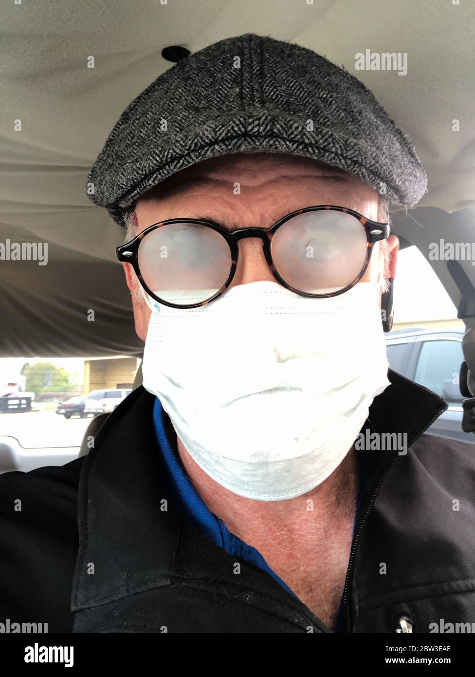 Uomo di mezza età in occhiali rotondi con cappuccio piatto grigio e maschera medica con occhiali foggati. Foto Stock