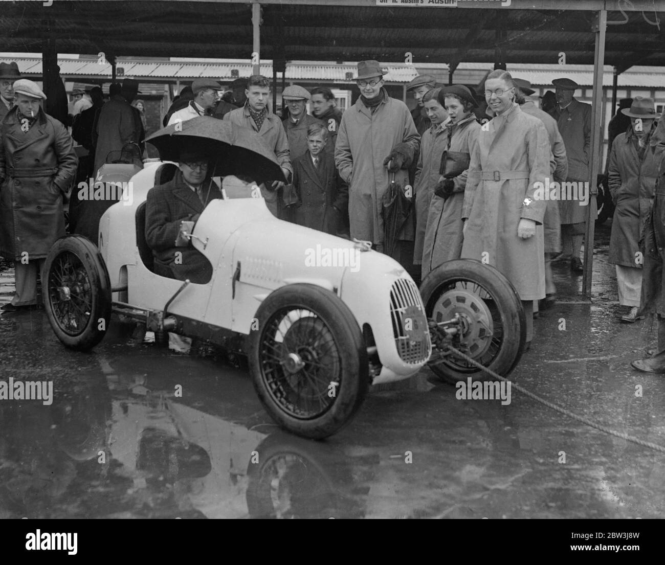 Ombrello come cappuccio a pioggia sodden Brooklands . La pioggia pesante ha causato la delusione a migliaia di appassionati di corse automobilistiche quando l'incontro del lunedì di Pasqua a Brooklands ha dovuto essere rinviato . Foto spettacoli , R A Jameson , designer del nuovo super carica Austin Seven , utilizzando un ombrello come ' cappuccio ' . 13 aprile 1936 Foto Stock