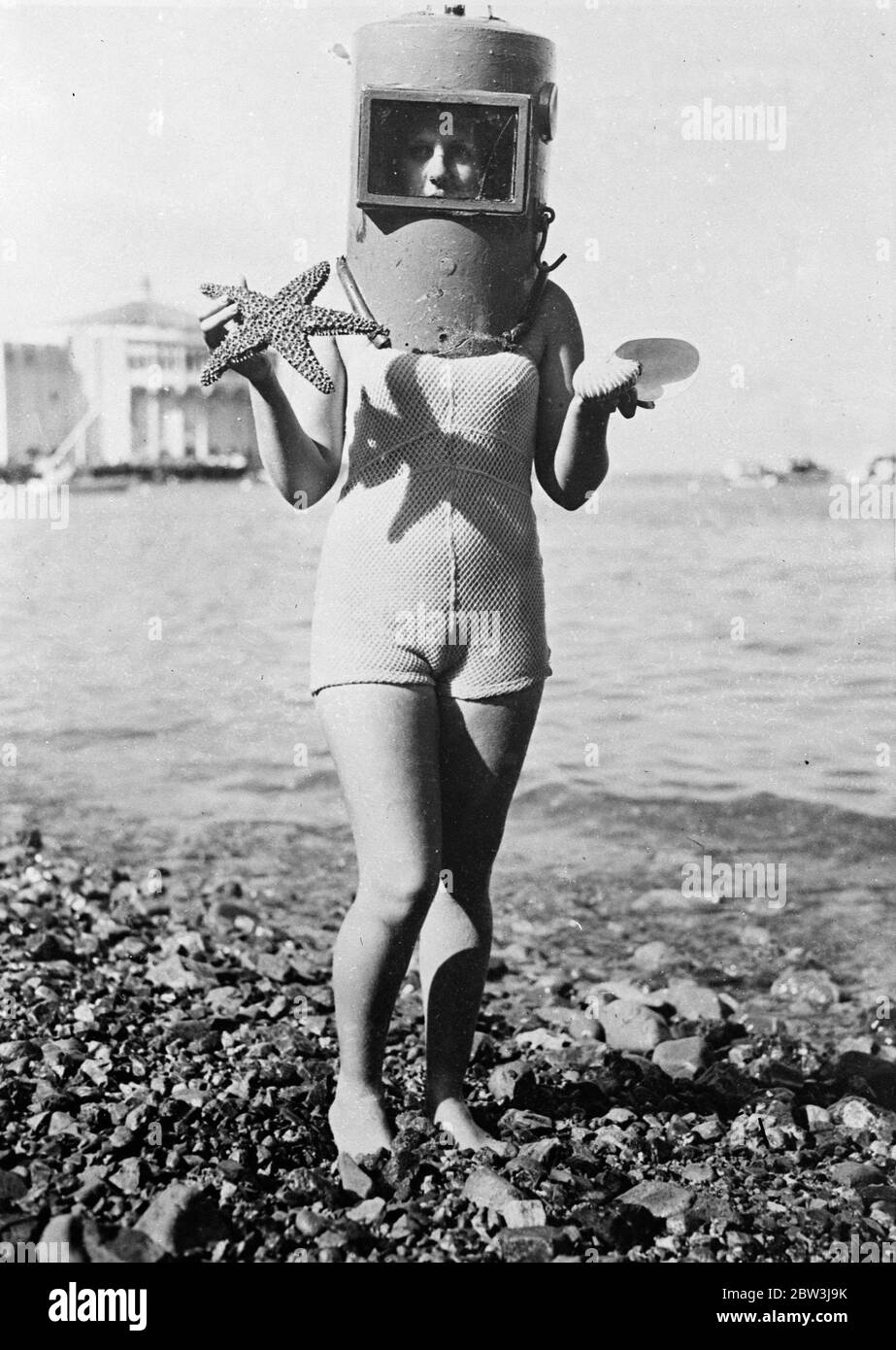 Figlia di Nettuno . Lei passeggerà sul letto di mare . I vacanzieri dell' Isola di Santa Catalina , USA , hanno ricevuto un nuovo brivido . I famosi giardini sottomarini che un tempo venivano ispezionati attraverso imbarcazioni con fondo in vetro possono ora essere visti in quartieri vicini . Dotato di un casco speciale per immersioni , i visitatori possono passeggiare tra i giardini e portare in superficie qualsiasi curiosa crescita marina che prenda la loro fantasia . Foto mostra , ancora indossando il suo casco speciale immersione una ragazza Santa Catalina , Nancy Harris , porta in superficie una stella marina e una conchiglia nautilus strappata dal fondale . 17 maggio 1936 Foto Stock