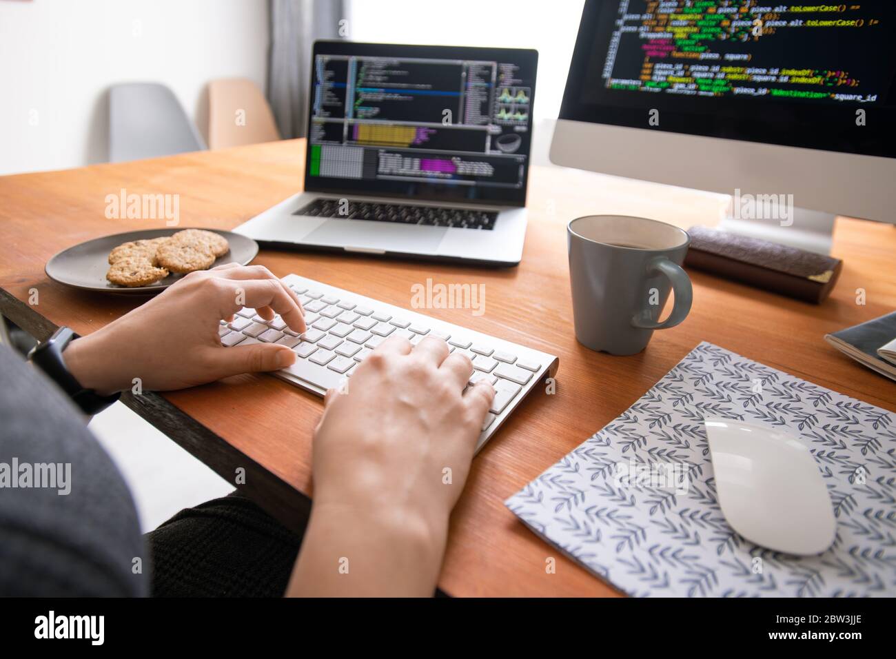 Primo piano di un programmatore irriconoscibile seduto alla scrivania con caffè e cookie e la creazione di codice per il software per computer Foto Stock