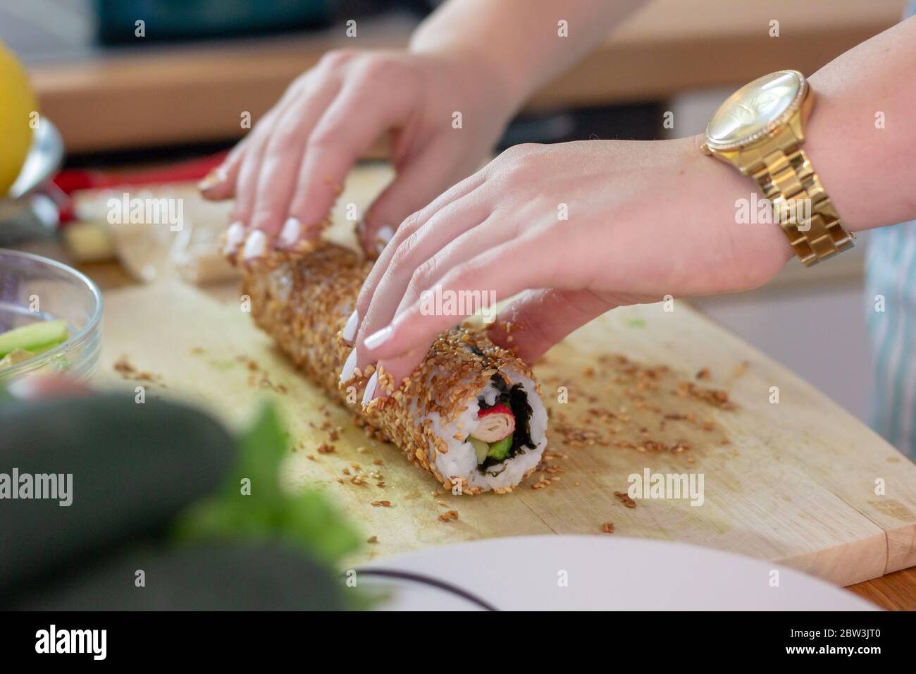 Mani femminili che rotola un sushi in semi di sesamo fritti. Preparare un piatto complicato come il sushi a casa Foto Stock