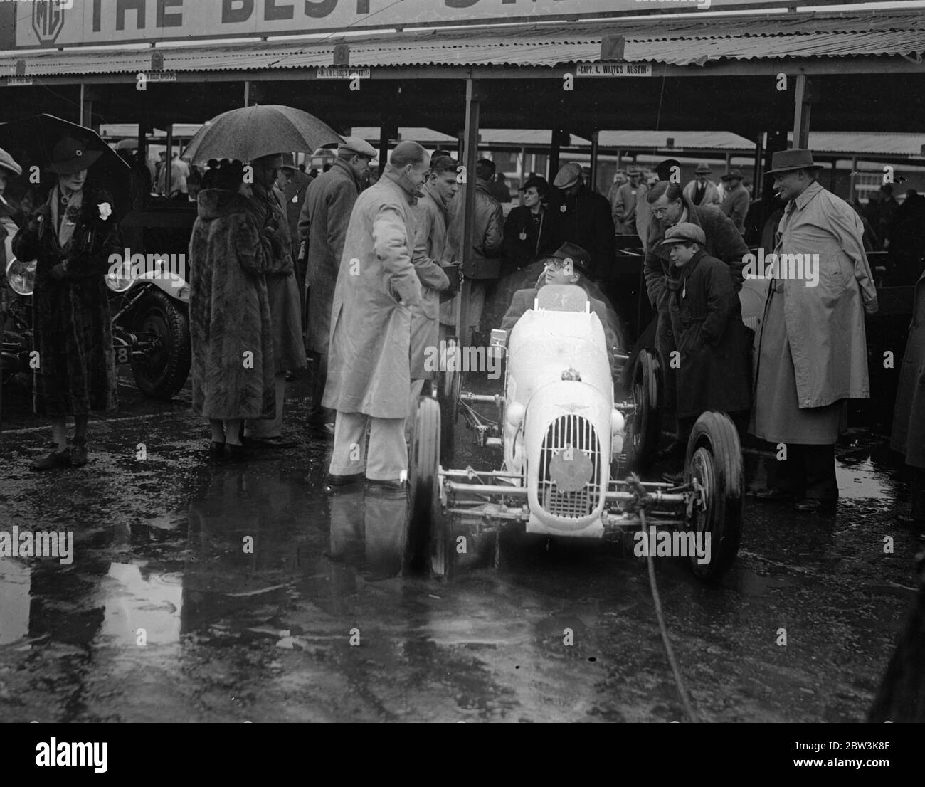 Ombrello come cappuccio a pioggia sodden Brooklands . La pioggia pesante ha causato la delusione a migliaia di appassionati di corse automobilistiche quando l'incontro del lunedì di Pasqua a Brooklands ha dovuto essere rinviato . Foto spettacoli , R A Jameson , designer del nuovo super carica Austin Seven , utilizzando un ombrello come ' cappuccio ' . 13 aprile 1936 Foto Stock