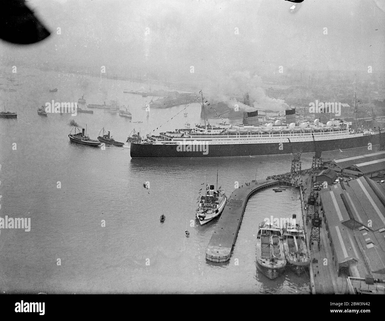 La ' RMS Queen Mary' salpa da Southampton in un viaggio da nubile. Allietato da un quarto di milione di persone che riempiono ogni pollice disponibile dei banchine . La Regina Mary, 80 anni, 000 e' orgogliosa della British Merchant Navy, salpò da Southampton in un suo primo viaggio in America. Era ' vestita su tutti ' con bandiere e centinaia di barche impavidite intorno a lei mentre si allontanava . Spettacoli fotografici , una vista aerea della 'RMS Queen Mary', lasciando i bacini di Southampton . 27 maggio 1936 Foto Stock